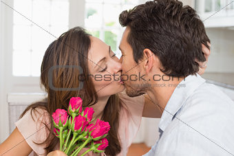 Loving couple kissing with flowers in hand at home