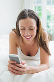 Smiling woman text messaging in bed