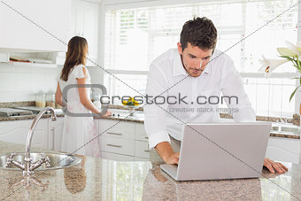 Man using laptop with woman in background at kitchen