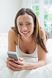 Smiling woman text messaging in bed