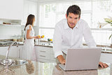 Man using laptop with woman in background at kitchen