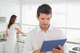 Man using digital tablet with woman in background at kitchen