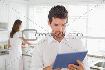 Man using digital tablet with woman in background at kitchen