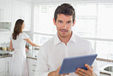 Man using digital tablet with woman in background in kitchen