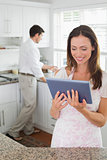 Woman using digital tablet with man in background in kitchen