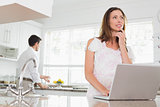 Woman using laptop with man in background in kitchen