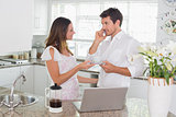 Couple having coffee with laptop on counter in kitchen