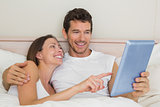 Happy couple using digital tablet in bed