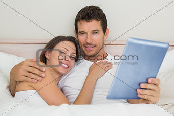 Happy couple using digital tablet in bed