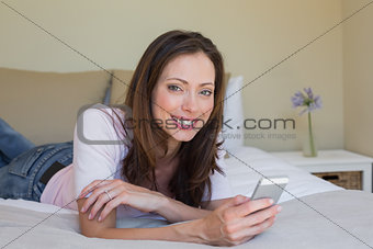 Smiling young woman text messaging in bed