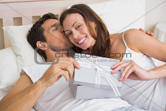 Relaxed couple with gift box lying together in bed
