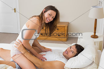 Young woman sitting on man in bed