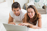 Smiling couple using laptop in bed