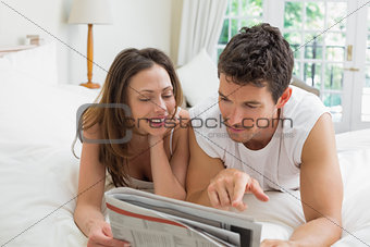 Relaxed couple reading newspaper in bed