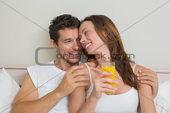Happy relaxed couple with orange juice in bed