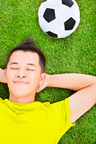 young man lying on a meadow with a football