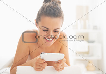 Smiling young woman laying on massage table and writing sms