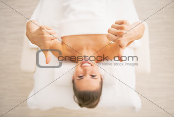 Closeup on smiling young woman laying on massage table and showi