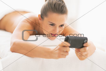 Young woman laying on massage table and writing sms