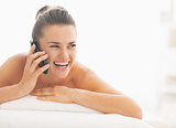 Young woman laying on massage table and talking mobile phone