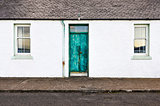 Green door and two windows on white wall house