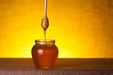 Honey jar with wooden dipper and flowing honey 