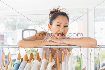 Beautiful female fashion designer with rack of clothes