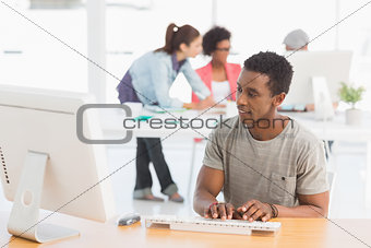 Male artist using computer with colleagues in background at office