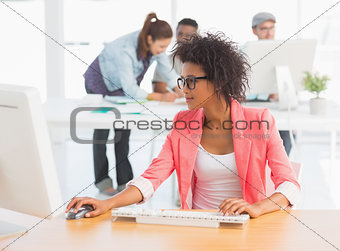 Female artist using computer with colleagues in background at office
