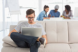 Man using laptop with colleagues in background at creative office