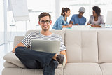 Man using laptop with colleagues in background at creative office