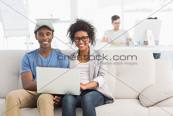 Couple using laptop with colleagues in background at creative office