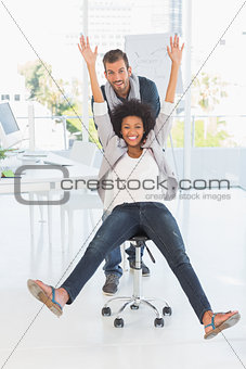 Playful young man pushing woman on chair in office