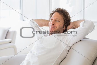 Relaxed man sitting with hands behind head at home