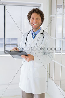 Happy handsome male doctor with clipboard in hospital