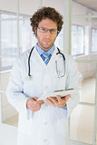 Serious male doctor standing with clipboard in hospital