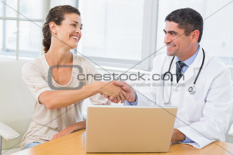 Doctor and patient shaking hands by laptop in office