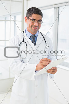 Smiling male doctor writing reports in hospital