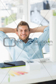 Handsome designer relaxing at his desk smiling at camera