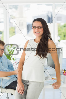 Brunette designer smiling at camera leaning on desk