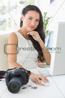 Focused photographer sitting at her desk using computer looking at camera