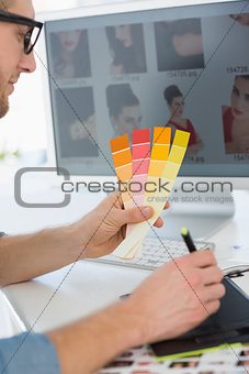 Handsome designer working with digitizer holding colour chart at his desk
