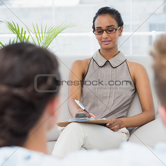 Therapist talking with couple on the couch and taking notes