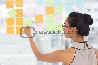 Smiling designer looking at sticky notes on window