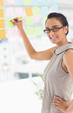Designer writing on sticky notes on window smiling at camera