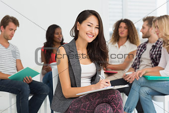 Smiling woman taking notes while colleagues are talking behind her