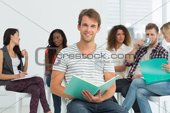 Smiling man taking notes while colleagues are talking behind him