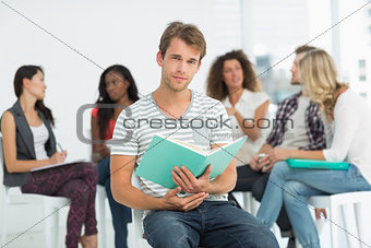 Happy man holding notebook while colleagues are talking behind him