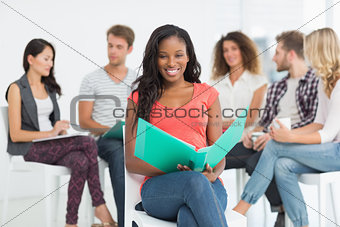 Smiling woman holding notebook while colleagues are talking behind her