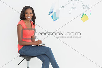 Smiling designer sitting and writing in front of whiteboard